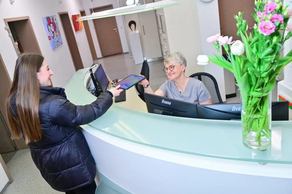 Eine Patientin übergibt ein Tablet an die Mitarbeiterin am Empfangstresen.