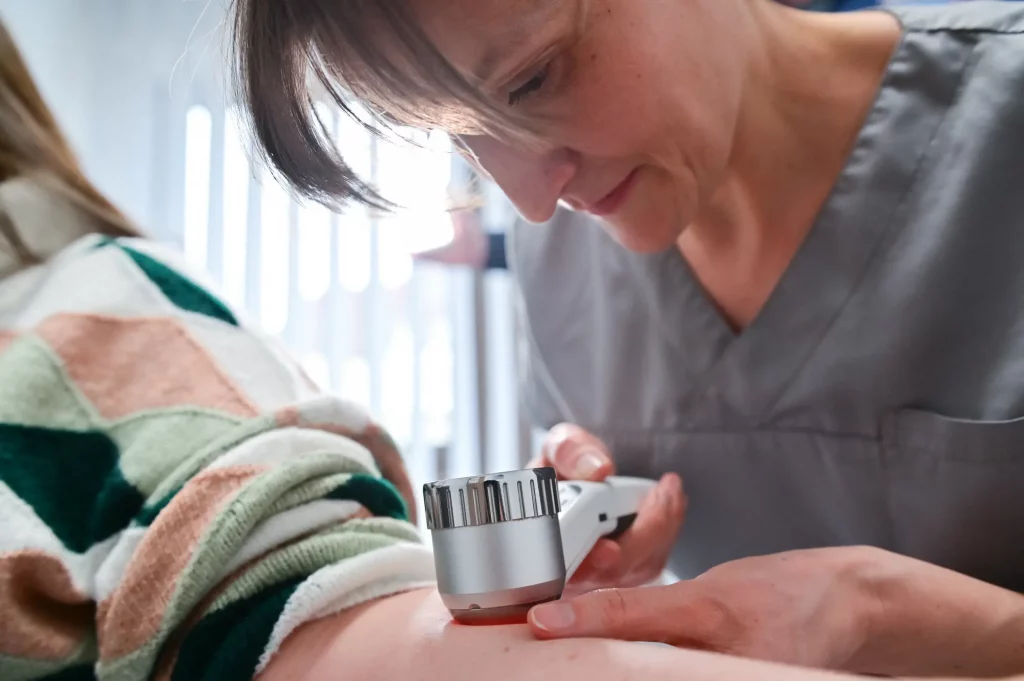 Ella Grosch untersucht den Arm einer Patientin mit einer Lupe.