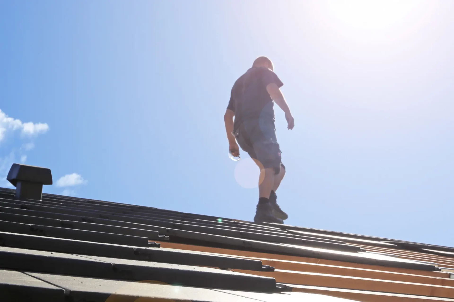 Ein Dachdecker bei Sonnenschein auf einem Hausdach.